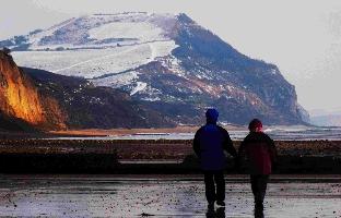 Couple walking on Charmouth beach in the late afternoon sunshine, with a snow Golden Cap behind them. Pic: Andy Morel.