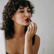 A woman putting on red lip stick. Credit: Canva