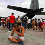 DEVASTATION: A survivor from Tacloban, which was devastated by Typhoon Haiyan gestures while sitting on the ground after disembarking an aircraft