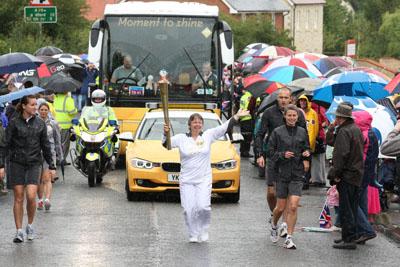 Marion Marchant carries the Olympic Flame on the Torch Relay leg between Milborne St Andrew and Dorchester. 