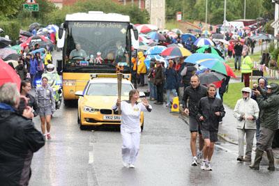 Marion Marchant carries the Olympic Flame on the Torch Relay leg between Milborne St Andrew and Dorchester. 