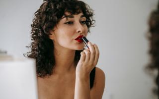 A woman putting on red lip stick. Credit: Canva