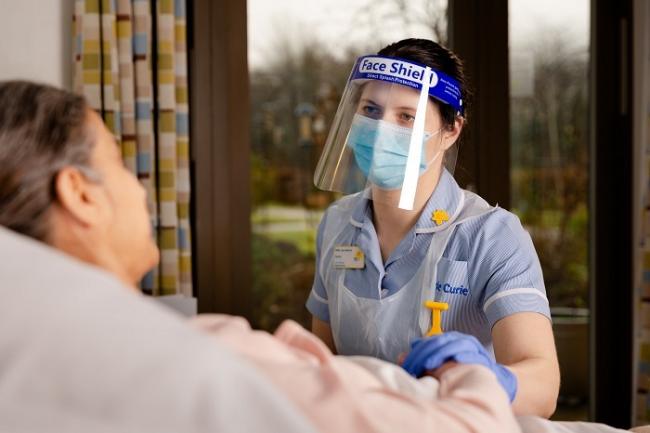 Laura Greensall, Marie Curie Nurse, in PPE, at the Marie Curie Hospice, West Midlands.....This picture was taken in January 2021 during the covid 19 pandemic.....Patient posed by a model.