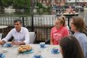 Rishi Sunak and the parliamentary candidate for Henley Caroline Newton (far right) speaking to rowing club members while Liberal Democrat supporters pass by on a boat, during a visit to the Leander Club in Henley-on-Thames, Oxfordshire (Jonathan