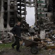 A young man pushes a wheelbarrow in front of a destroyed apartment building in the town of Borodyanka, Ukraine, on Sunday, April 10, 2022. Several apartment buildings were destroyed during fighting between the Russian troops and the Ukrainian forces